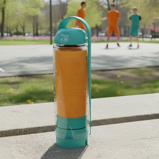 Turquoise koor refillable bottle on a concrete surface with people playing soccer in the background.