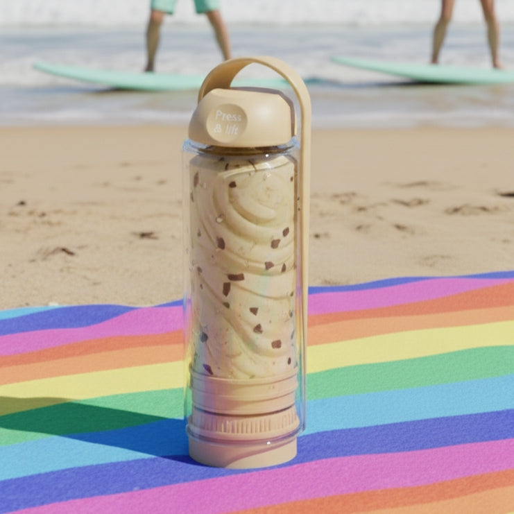 koor refillable bottle with beige lid and patterned sleeve on a colorful beach mat with people and surfboards in the background.